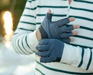 man wearing gloves, standing on boat deck in the evening sunshine.