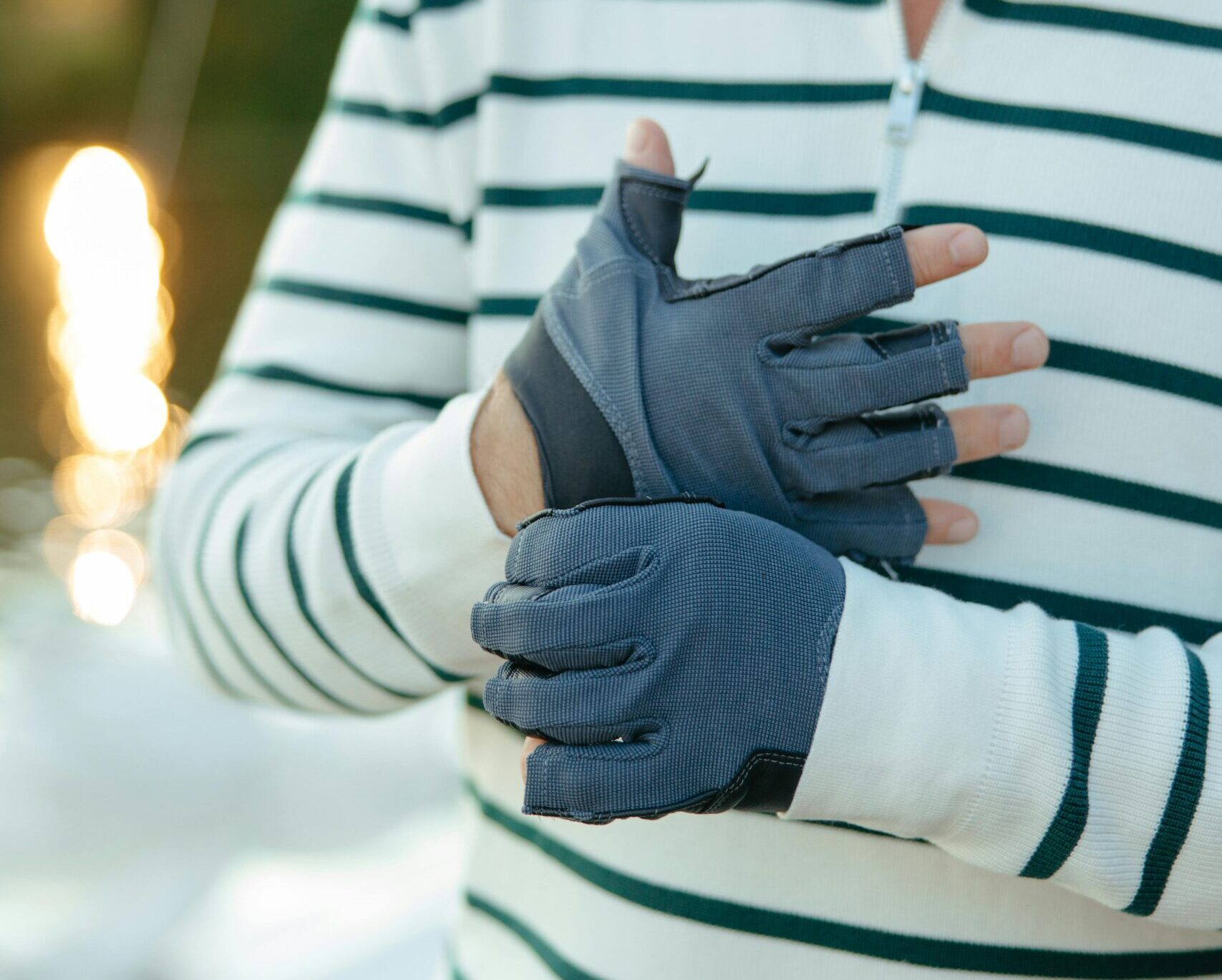 man wearing gloves, standing on boat deck in the evening sunshine.